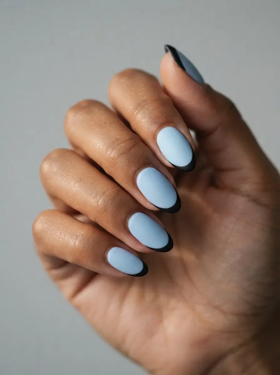 Baby blue nails with matte black crescent tips on warm brown skin