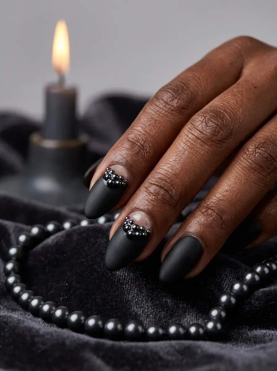 Nails with small black pearl beads sealed near the cuticle over a matte black base on deep brown skin