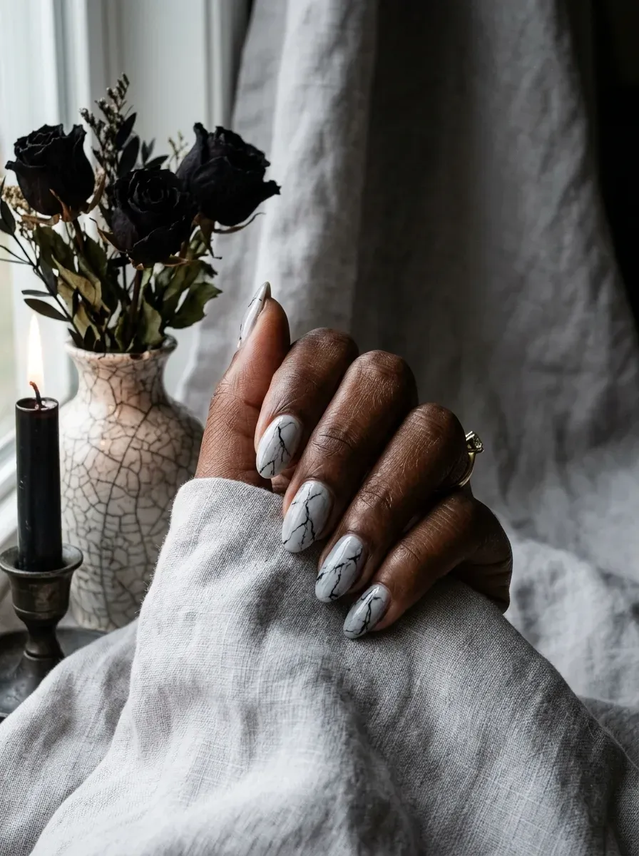Close-up of black vein marbling nail art over pale grey base on deep brown skin