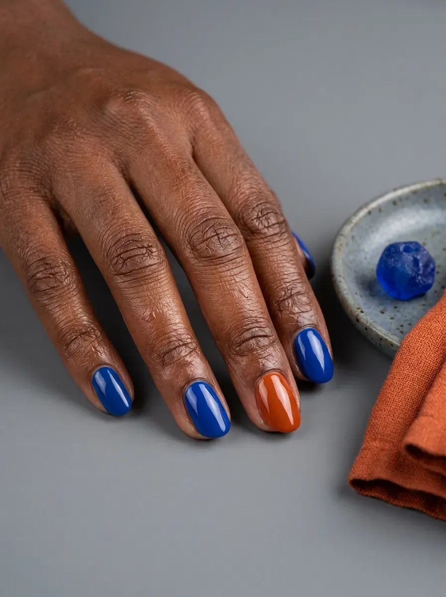 Nails alternating between solid cobalt blue and burnt orange polish on deep brown skin