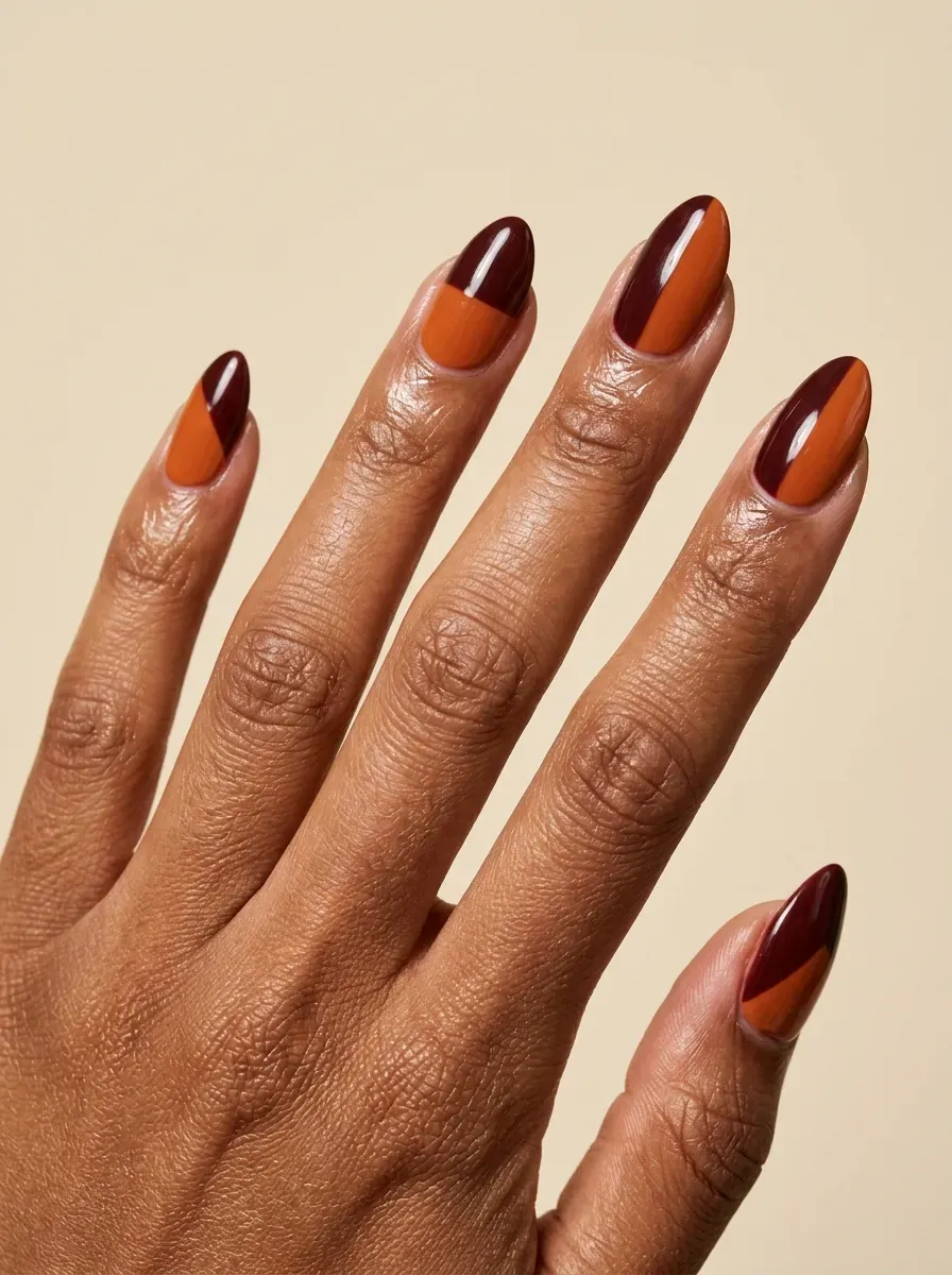 Almond gel nails with burgundy and burnt orange color blocking on warm skin