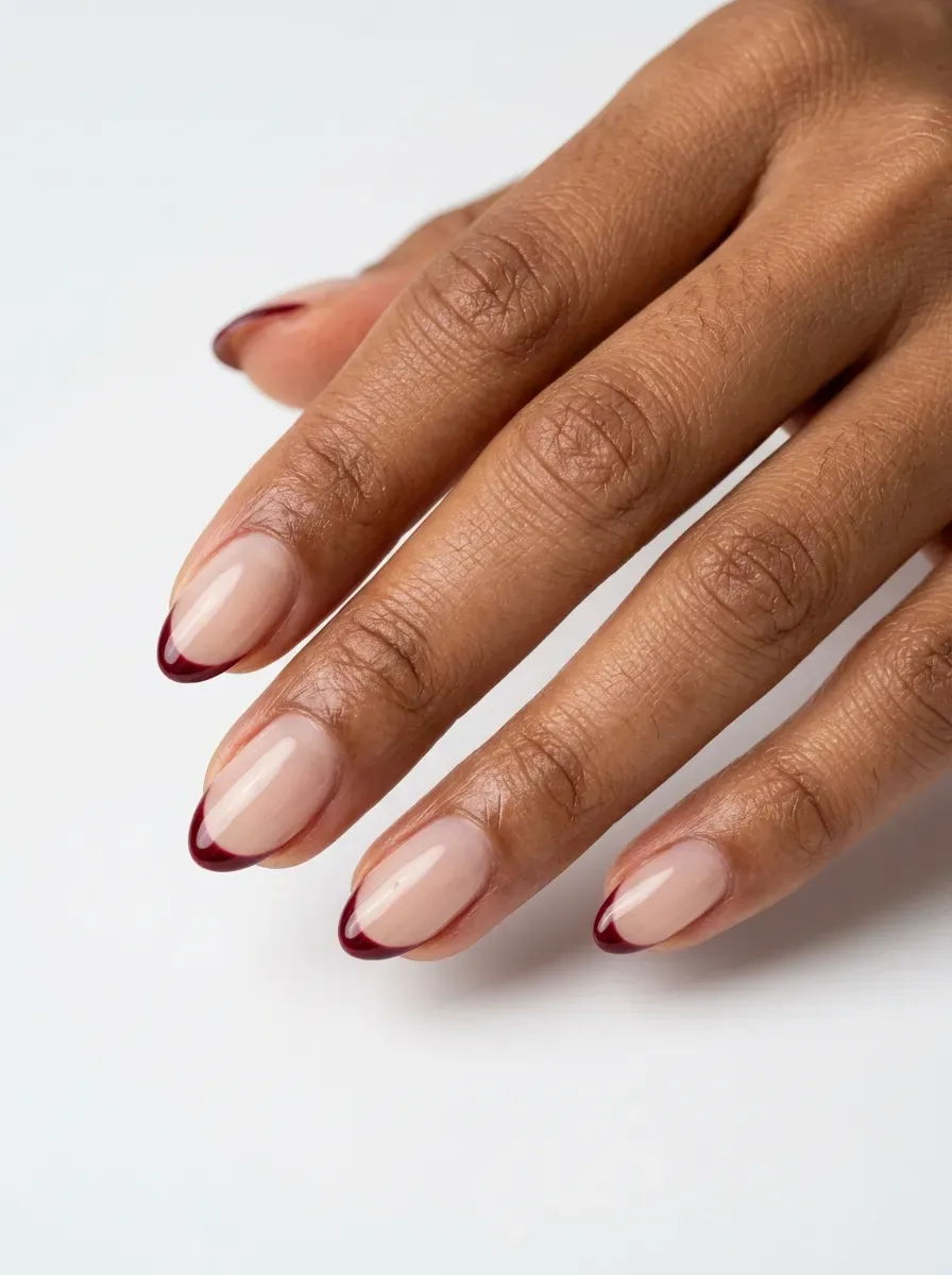Short almond nails with burgundy micro French tips on warm brown skin