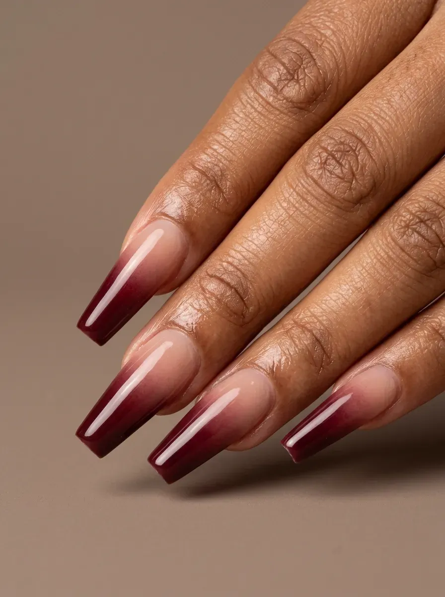 Long coffin nails fading from nude into glossy burgundy gel on brown skin