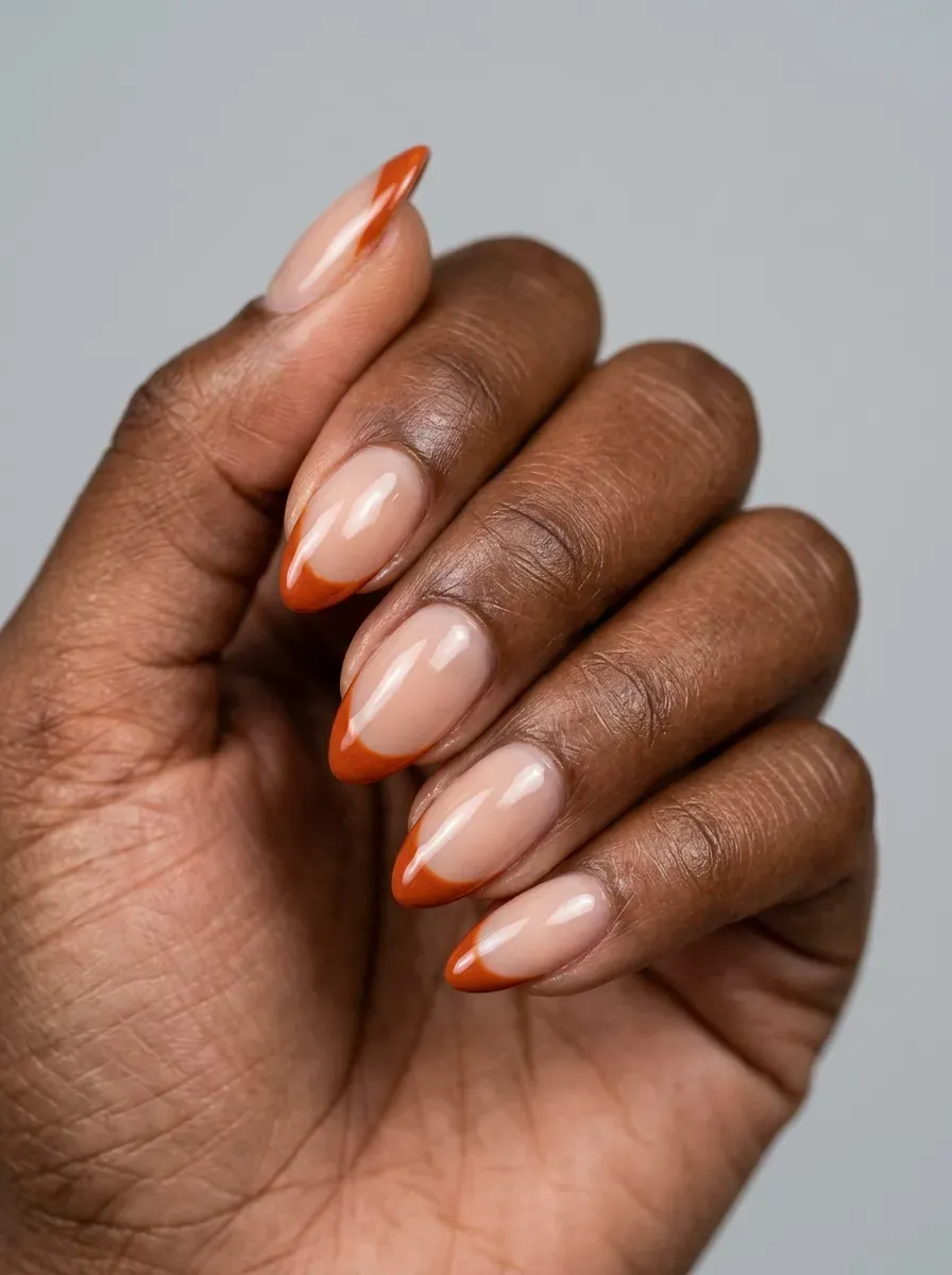 Almond nails with thin burnt orange French tips on deep chestnut skin