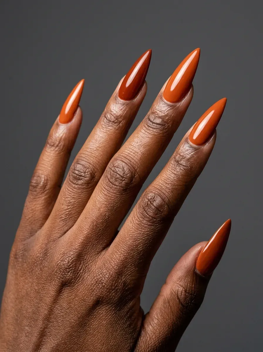 Burnt orange manicure with dramatic stiletto-shaped accent nails and glossy finish