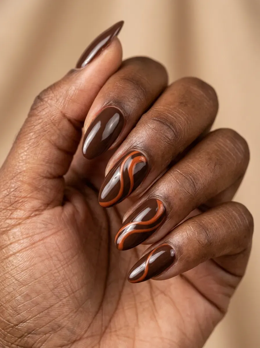 Glossy brown gel nails with burnt orange swirl accents on deep brown skin