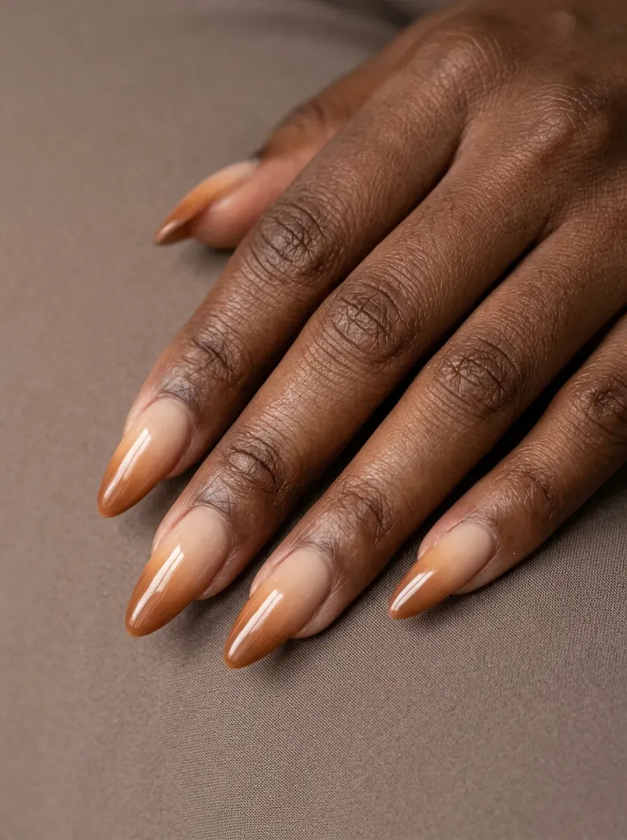 Long almond nails fading from nude into caramel brown gel on rich skin