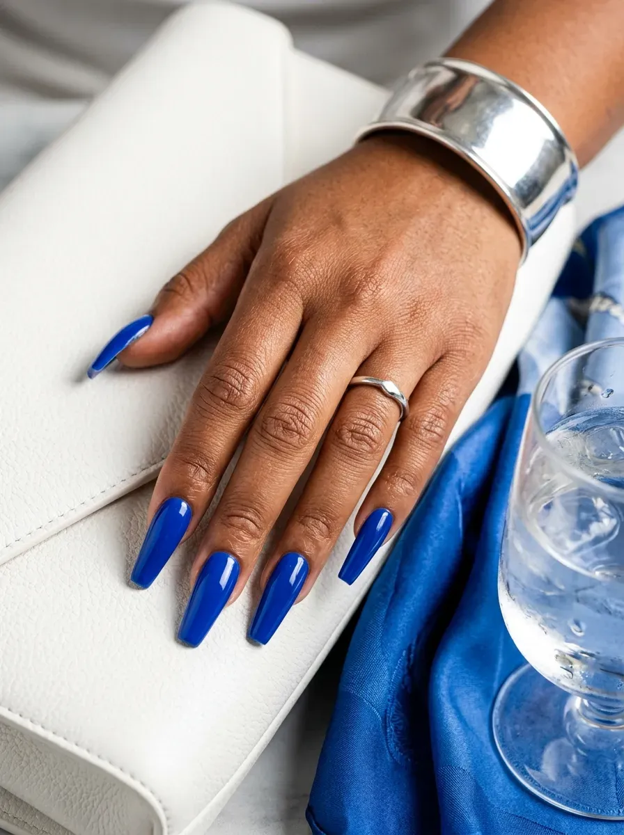 Long coffin nails painted glossy cobalt blue on warm brown skin