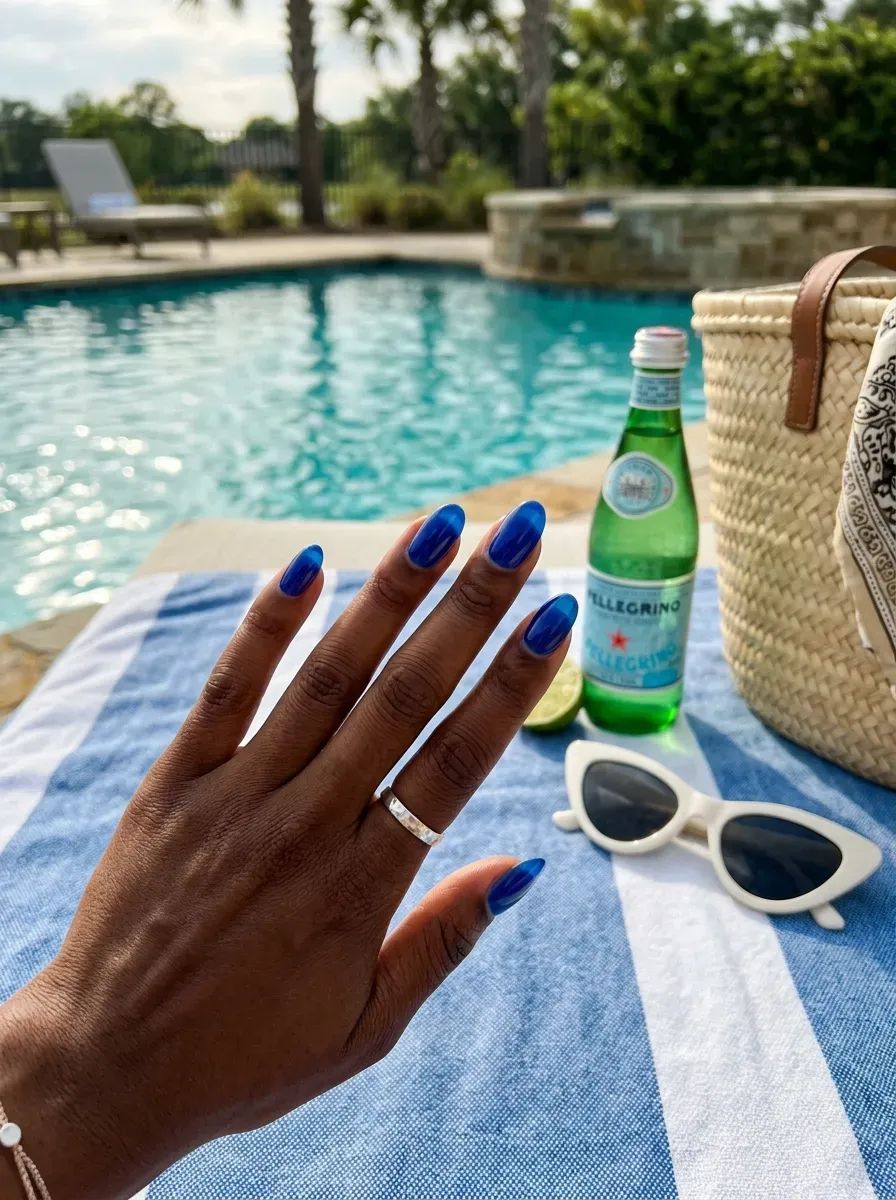 Translucent cobalt blue oval nails on deep brown skin beside pool accessories