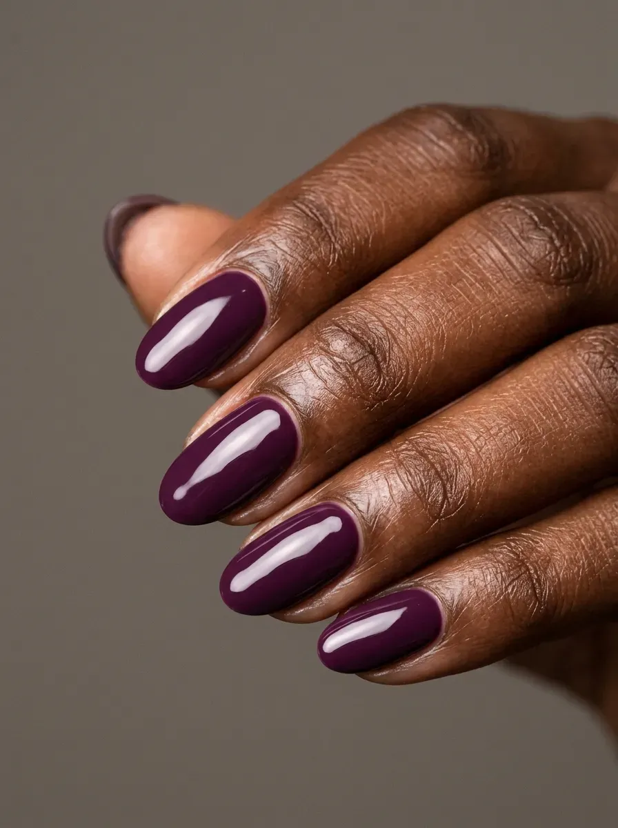Medium oval nails with deep plum glossy gel polish on rich dark skin