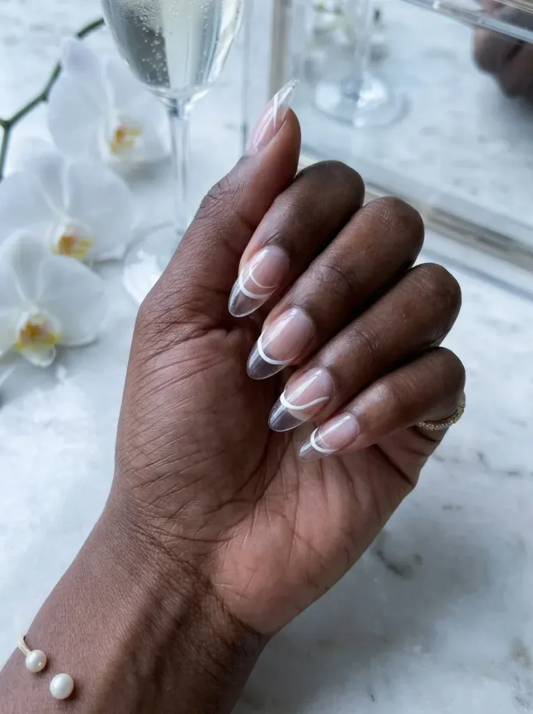 White curved lines floating above clear French tips on almond nails