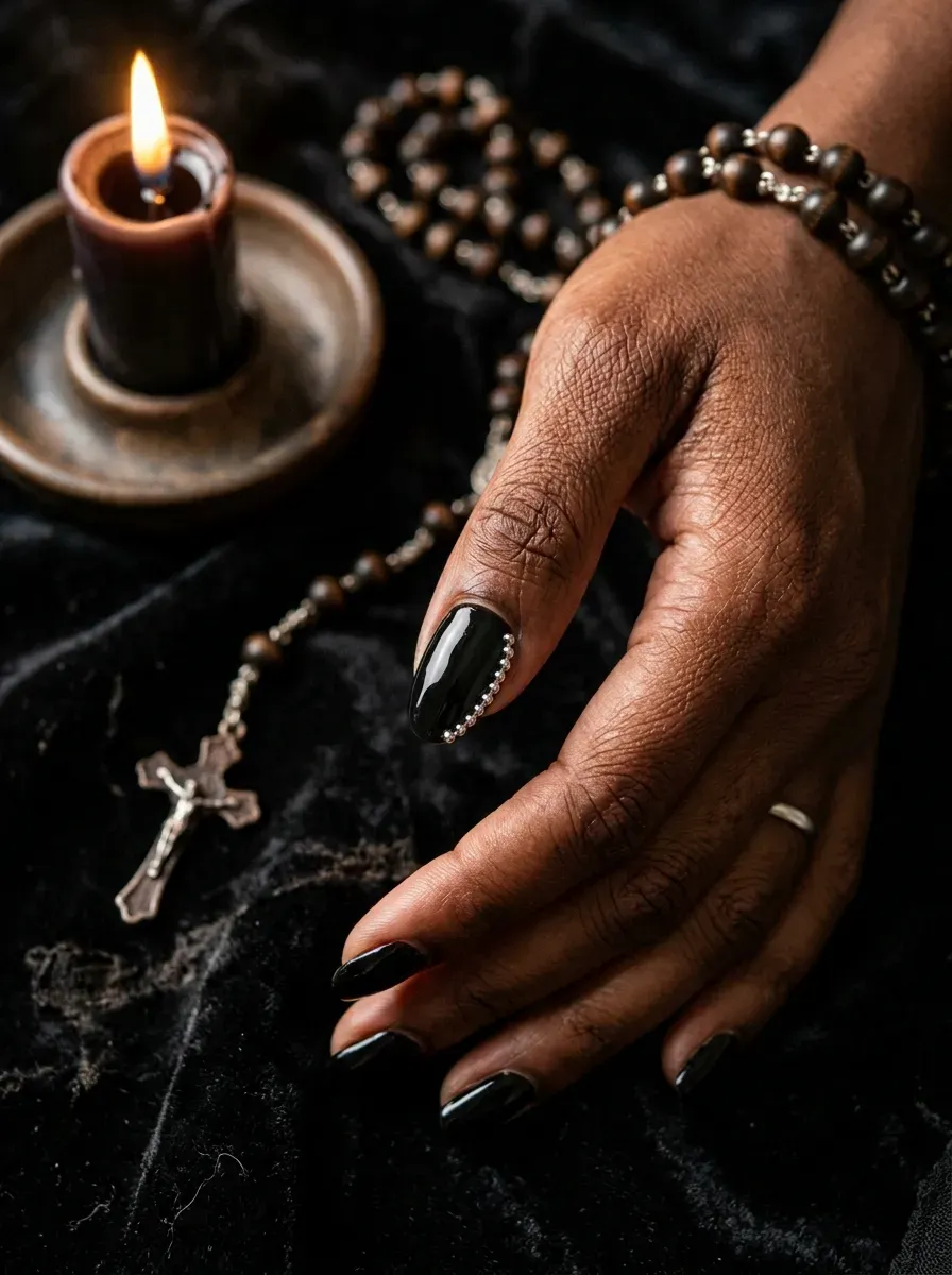 One black accent nail with small silver rosary bead charms sealed along the edge on deep brown skin