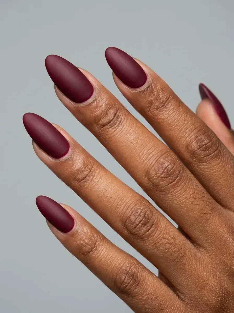 Long almond nails with smooth matte burgundy gel polish on brown skin