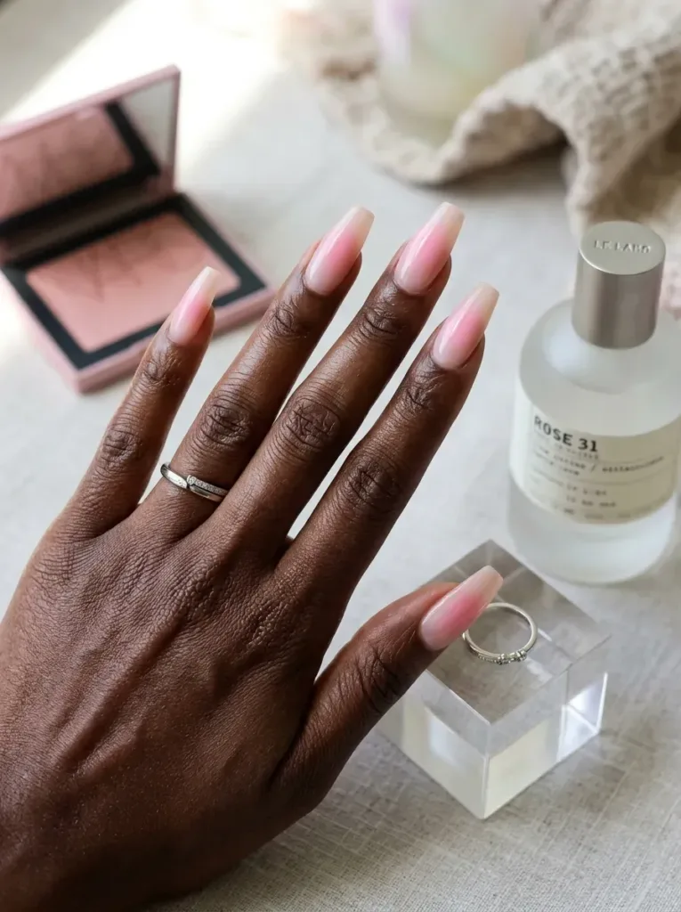 Long nude coffin nails with soft pink aura gradients on dark skin