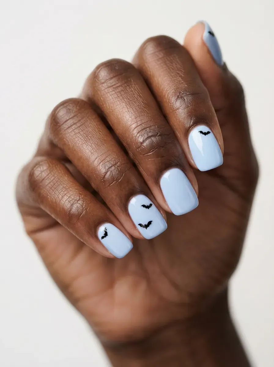 Powder blue nails with tiny black bat silhouettes on rich dark skin
