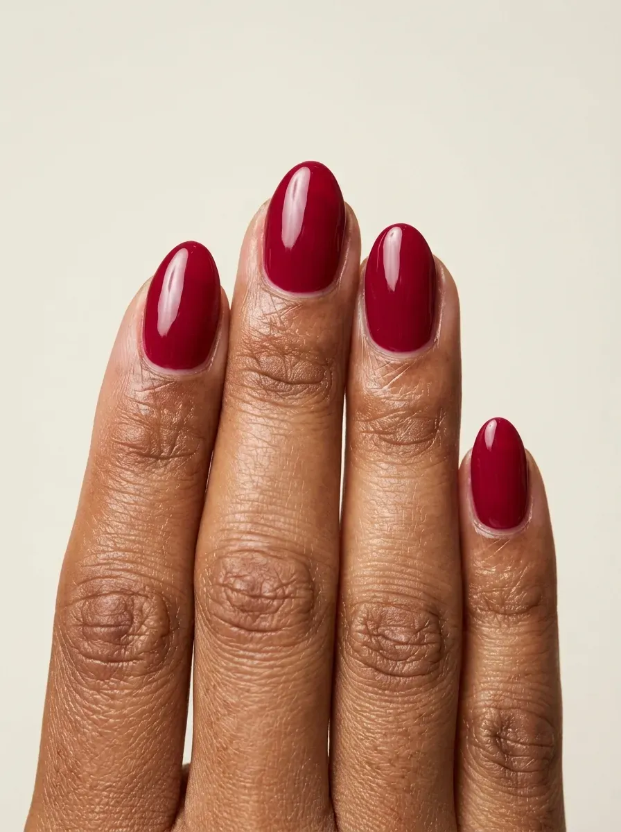 Short almond gel nails coated in glossy deep cranberry red polish