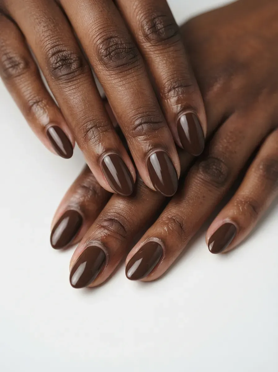 Short rounded nails with muted burnt orange French tips on warm brown skin