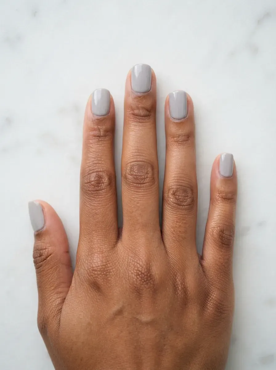 Close-up of short squoval nails in light dove gray creme on warm brown skin