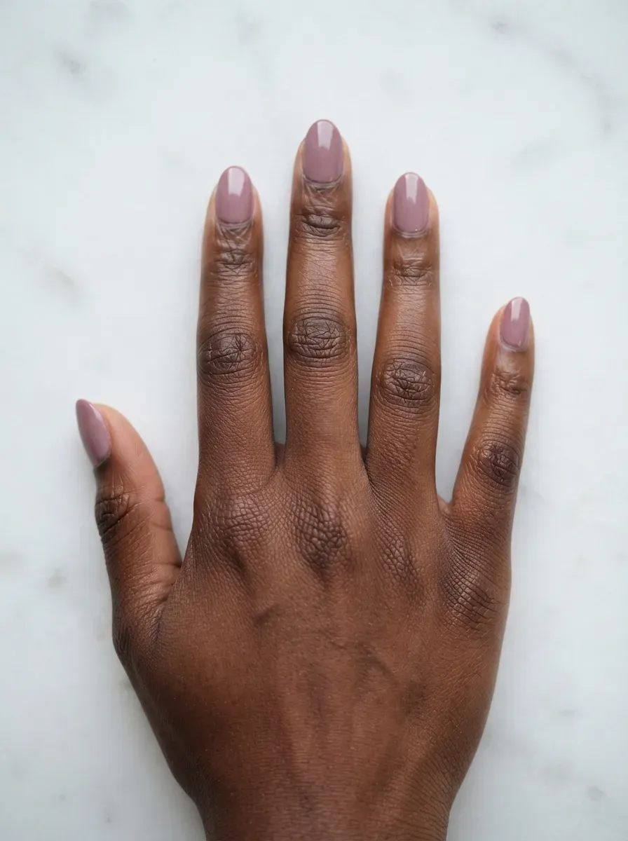 Close-up of short almond nails in muted mauve creme polish on deep brown skin