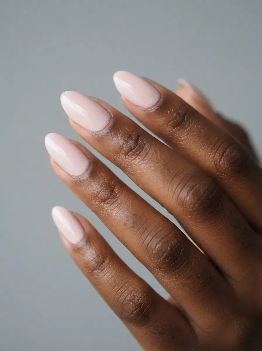 Close-up of short almond nails in pale rose creme polish on deep brown skin