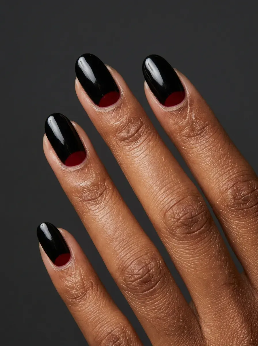 Black nails with deep red crescent moon accents near the cuticles