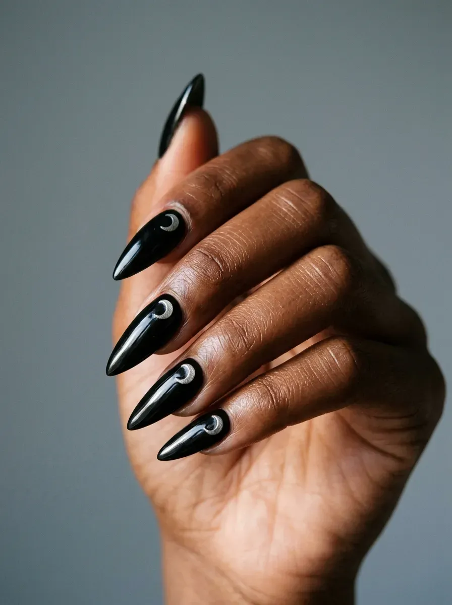 Glossy black stiletto nails with tiny silver crescent moon accents