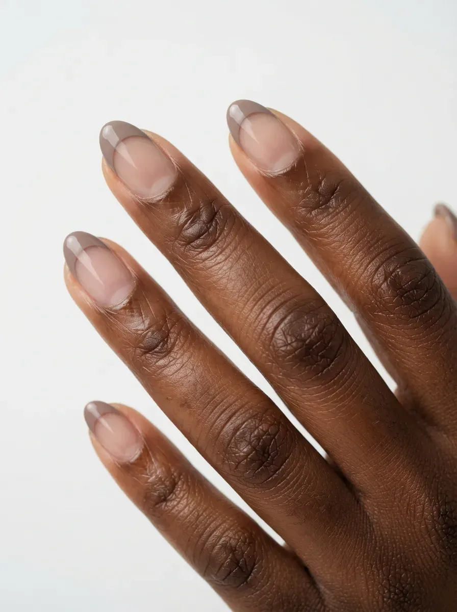 Short almond nails with taupe French tips and negative space on deep skin
