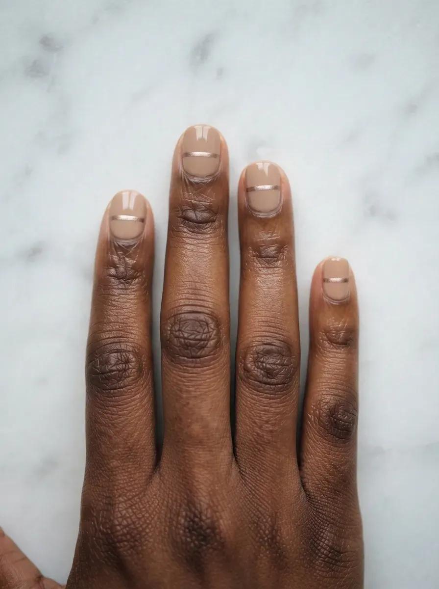 Close-up of short nails with thin champagne metallic line detail on rich dark skin tone